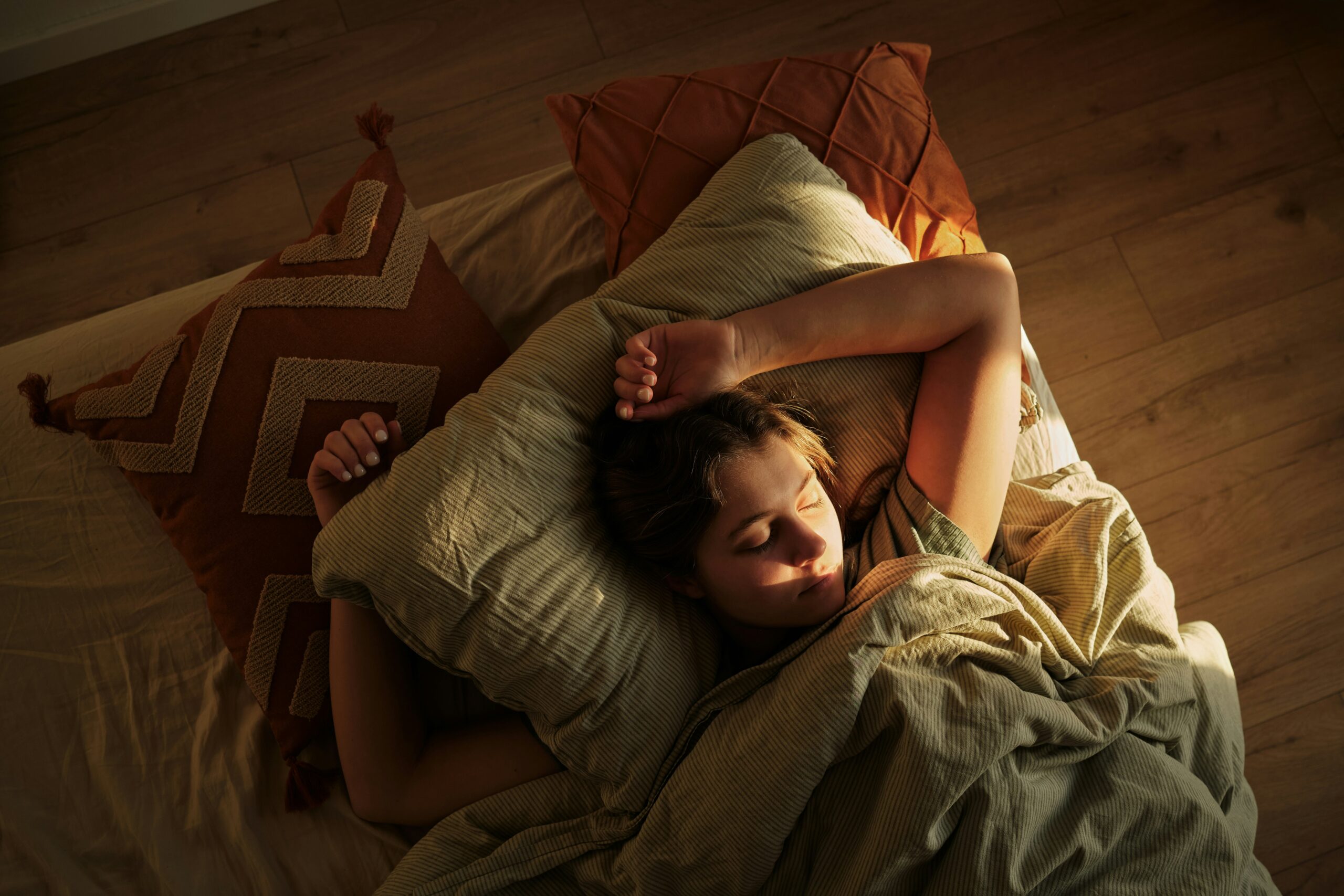pessoa deitada na cama com os braços acima da cabeça, enquanto um fecho de luz reflete em seu rosto